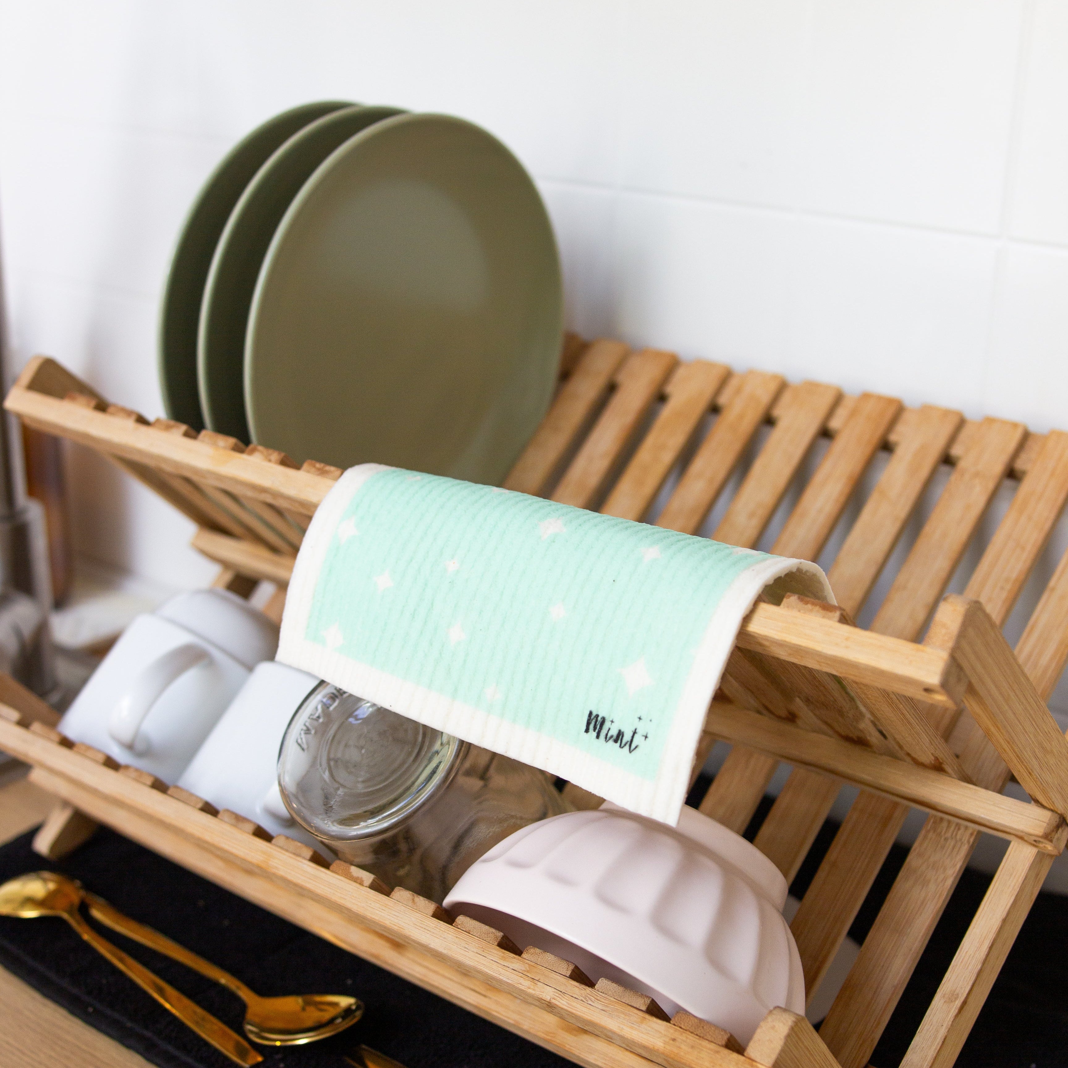 Wooden dish rack with plates, mugs, and a dishcloth on a wooden surface.