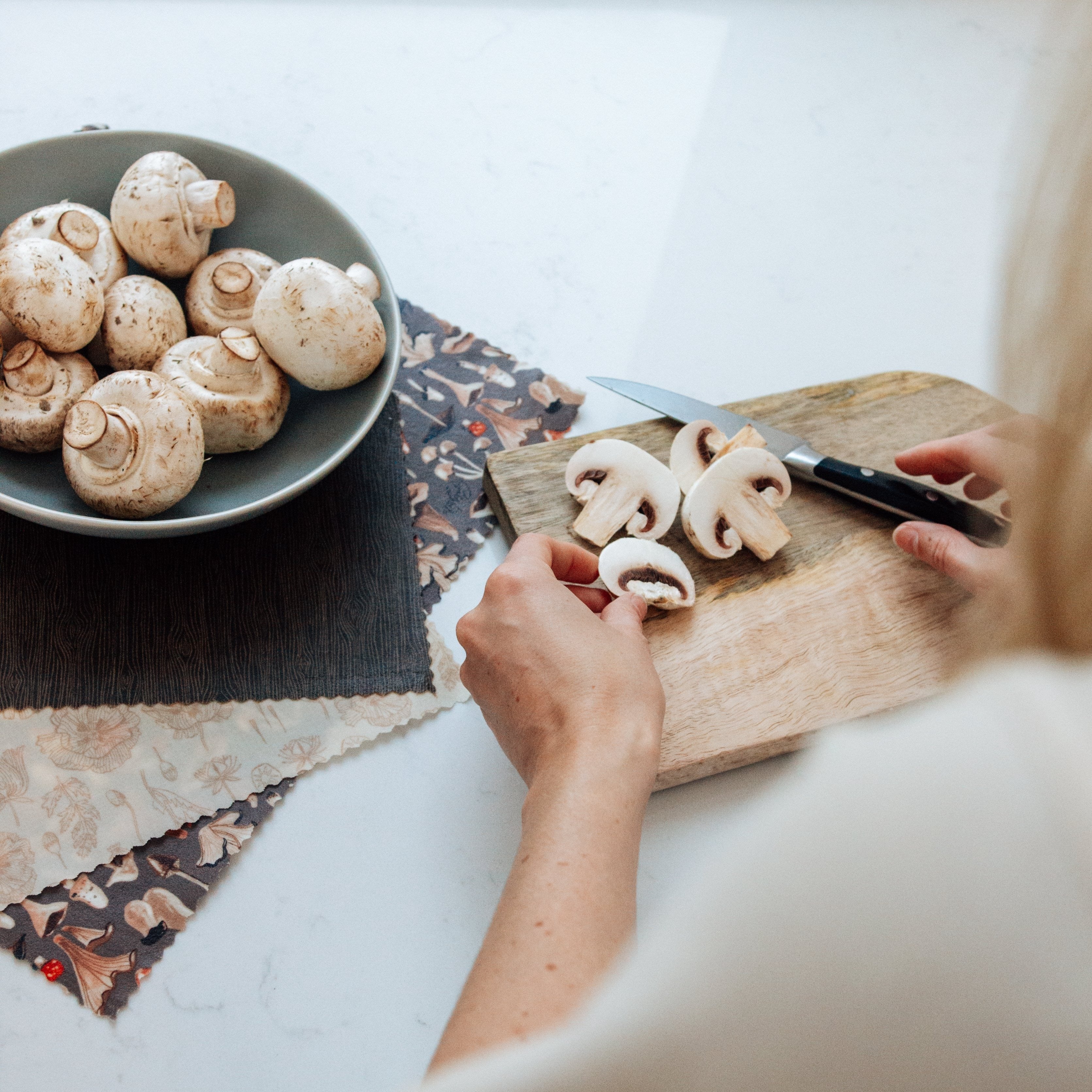 Mushrooms being cut on a cutting board placed beside a set of 3 mushroom beeswax wraps