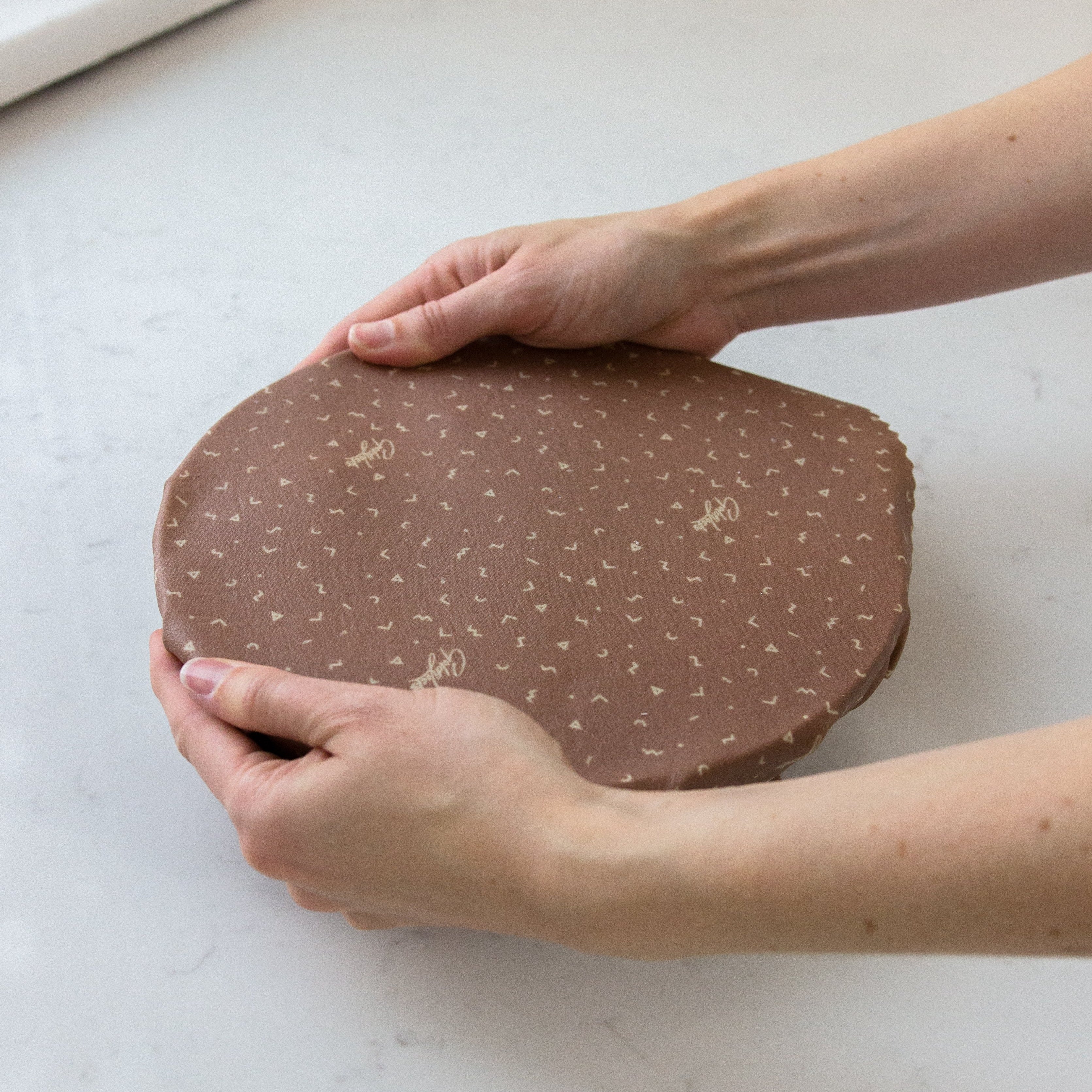 Taupe beeswax wrap covering pasta bowl using heat of hands to create seal
