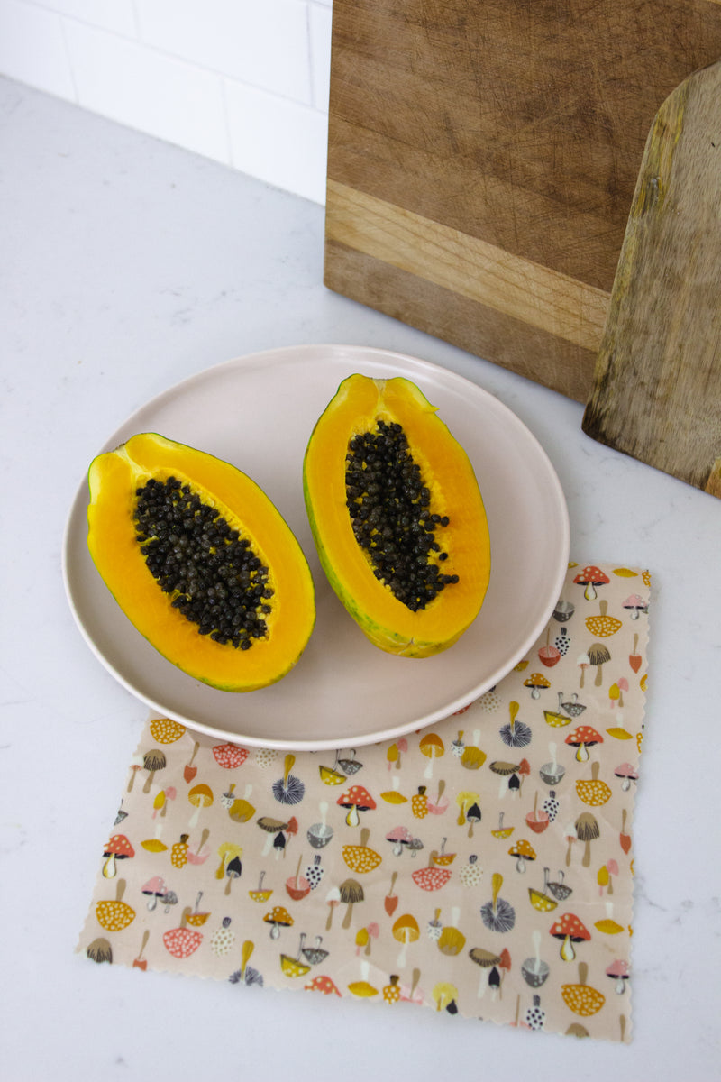 a papaya cut in half placed on top of brightly coloured medium beeswax wrap featuring different types of mushrooms