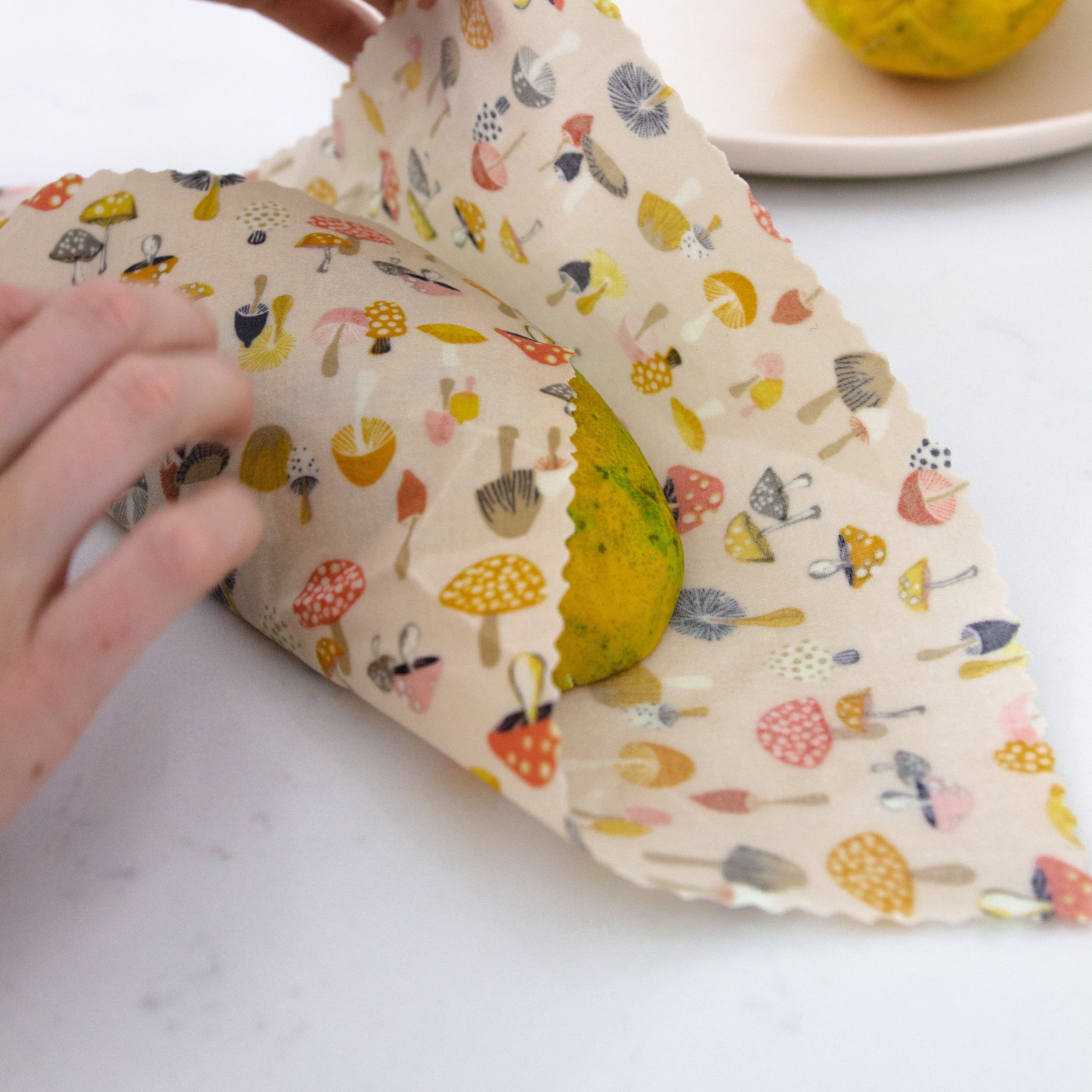 a medium mushroom beeswax food wrap covering one half of a papaya
