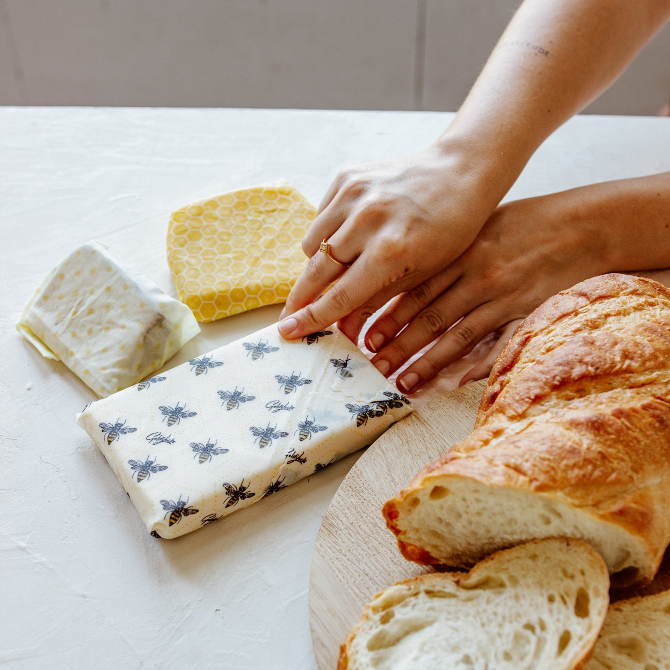 Person arranging bread slices on a wooden board with cheese blocks wrapped in beeswax wraps with bee themed patterns
