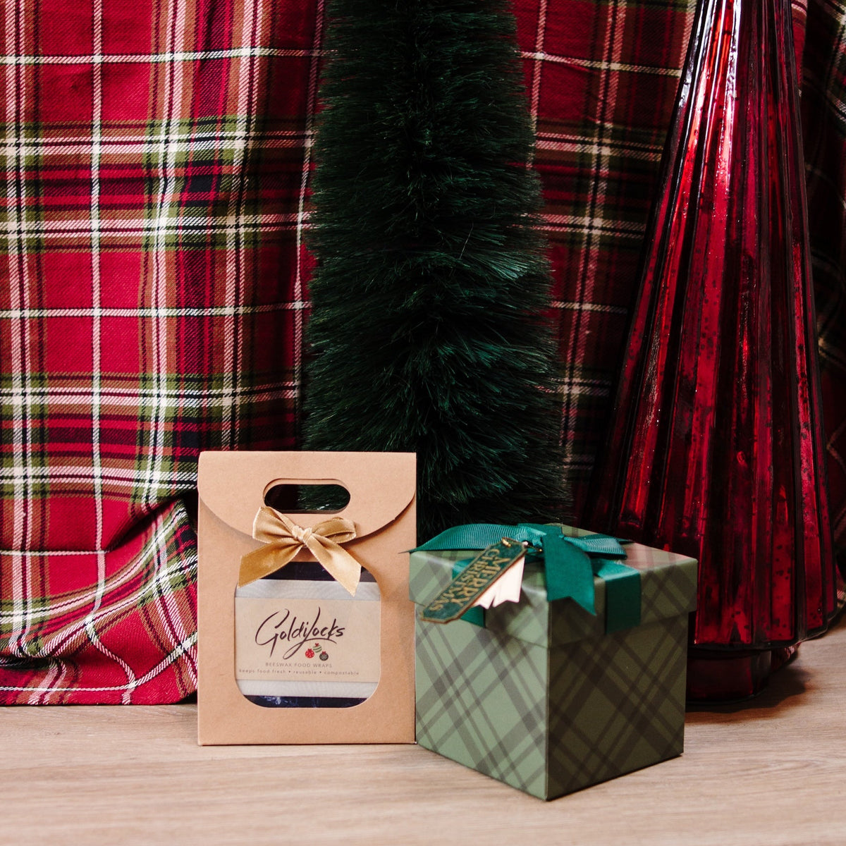 holiday gift set of beeswax wraps placed in a kraft paper package. Red plaid background with holiday trees and gifts