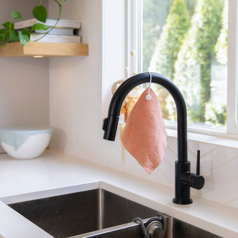 Modern kitchen sink with black faucet and pink dishcloth, natural light from window.
