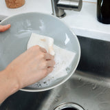swedish dishcloth being used to wash a pasta bowl in the kitchen sink