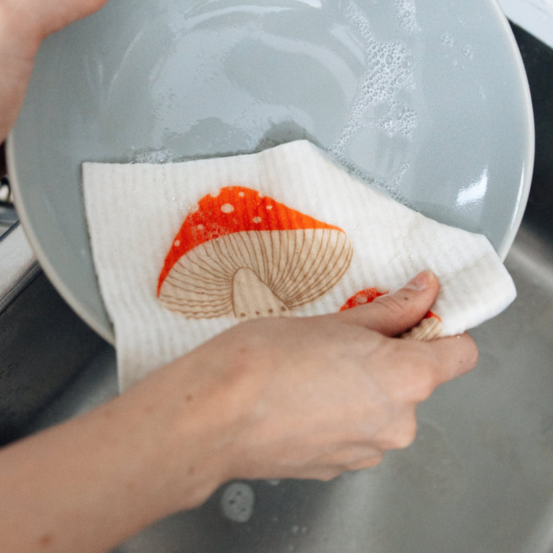 mushroom swedish dishcloth being used to wash a grey pasta bowl covered in soap suds