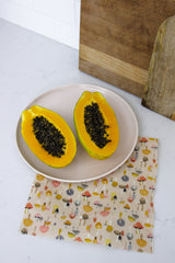 a papaya cut in half placed on top of brightly coloured medium beeswax wrap featuring different types of mushrooms