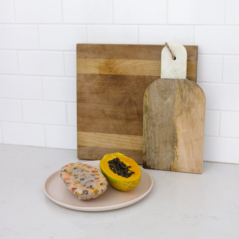 two cutting boards behind a papaya cut in half wrapped in a medium beeswax wrap with mushrooms printed on it