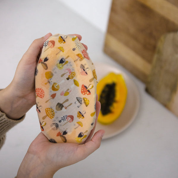 a colourful mushroom print beeswax wrap covering a halved papaya